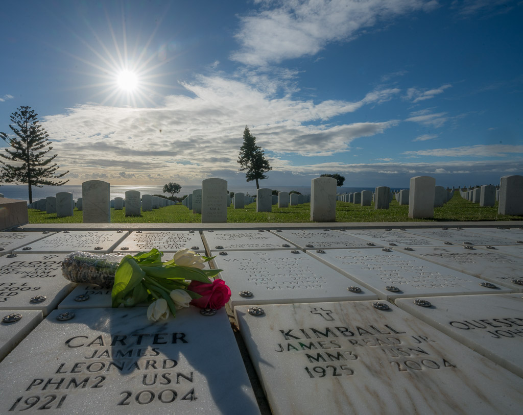 Military cemetery at Cabrillo National Monument San Diego - Marble plate with names of fallen soldiers with a single red rose and the rows of graves with white stones in the background overlooking the Pacific ocean