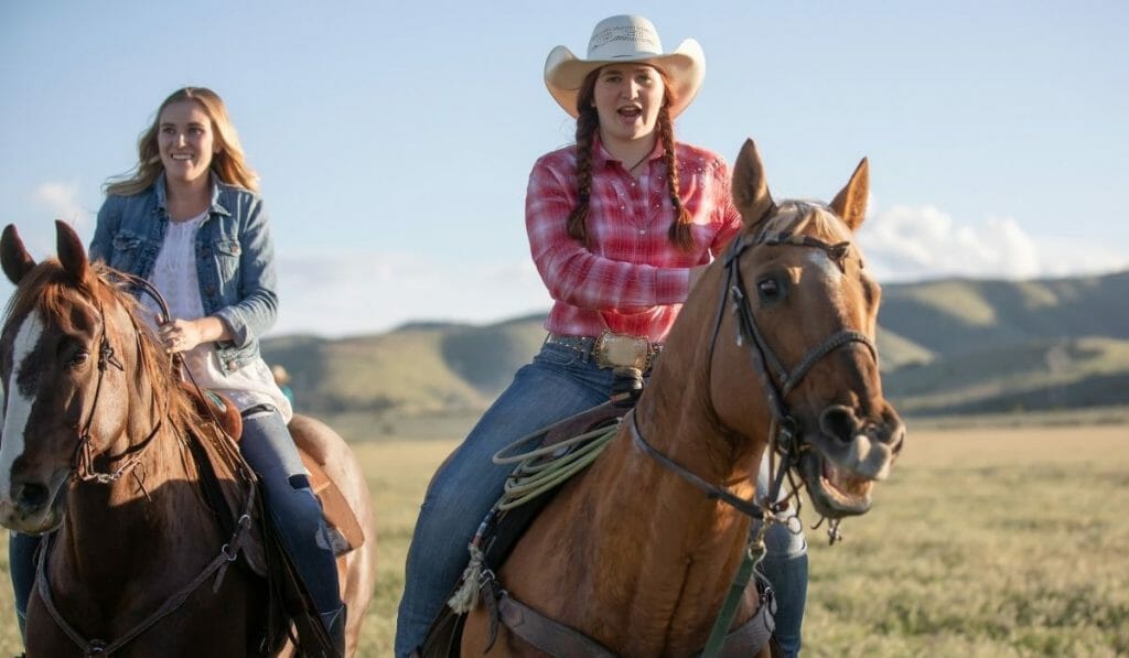 Two young women riding horses over grassy hills