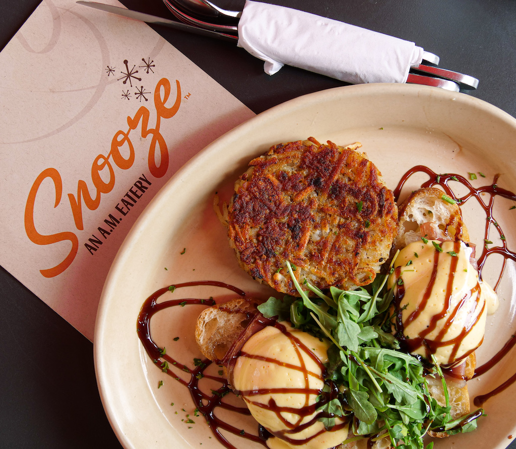 Eggs benedict with an interesting twist with a side of hasbrowns next to a Snooze menu