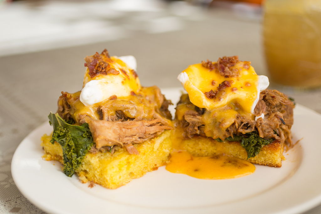 An eggs benedict on a sweet roll with pork and greens