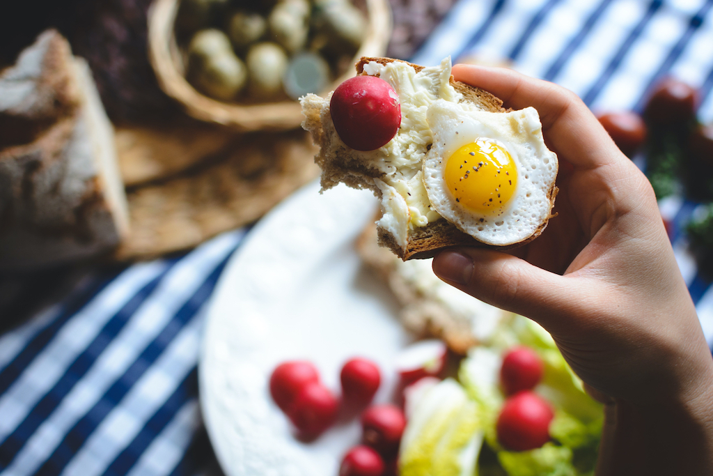 A quail egg and a radish on top of buttered toast with a few bites taken out of it