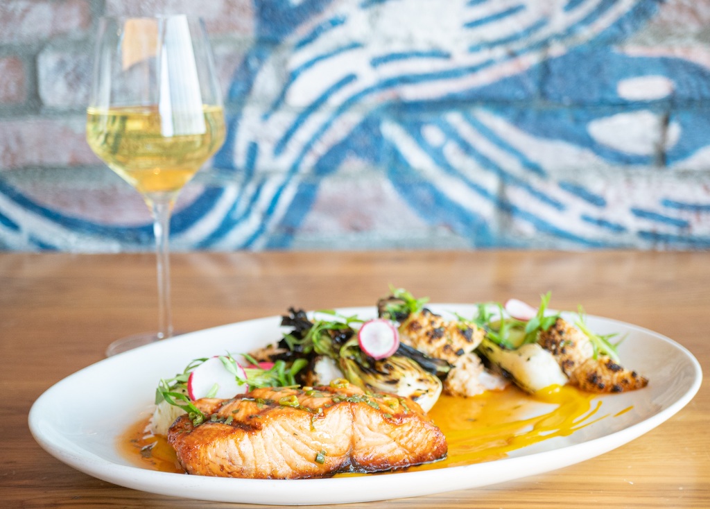 Salmon with radishes and other seafood in a yellow sauce paired with a white wine