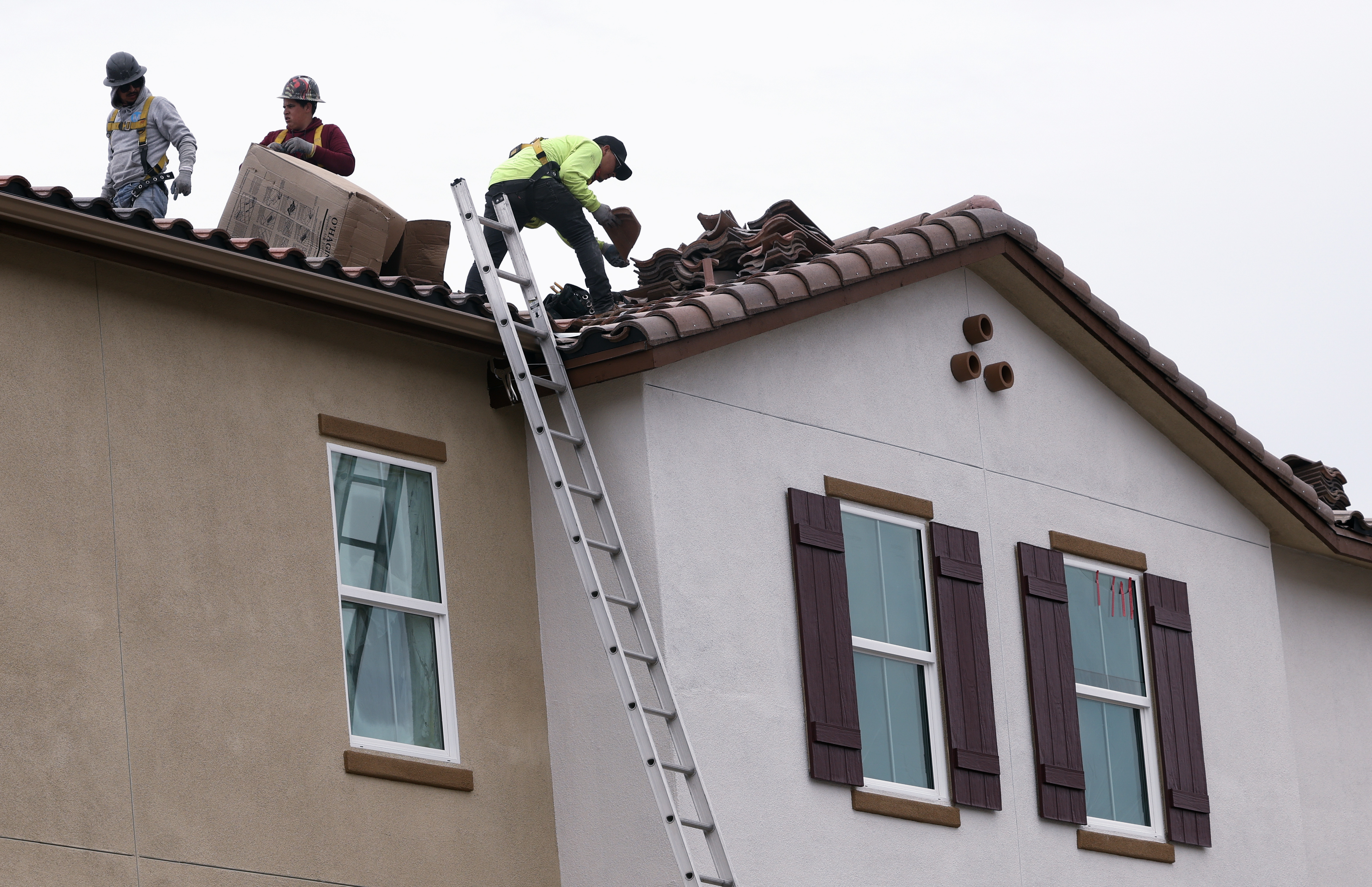 Workers place roof tiles on the roof of one of...