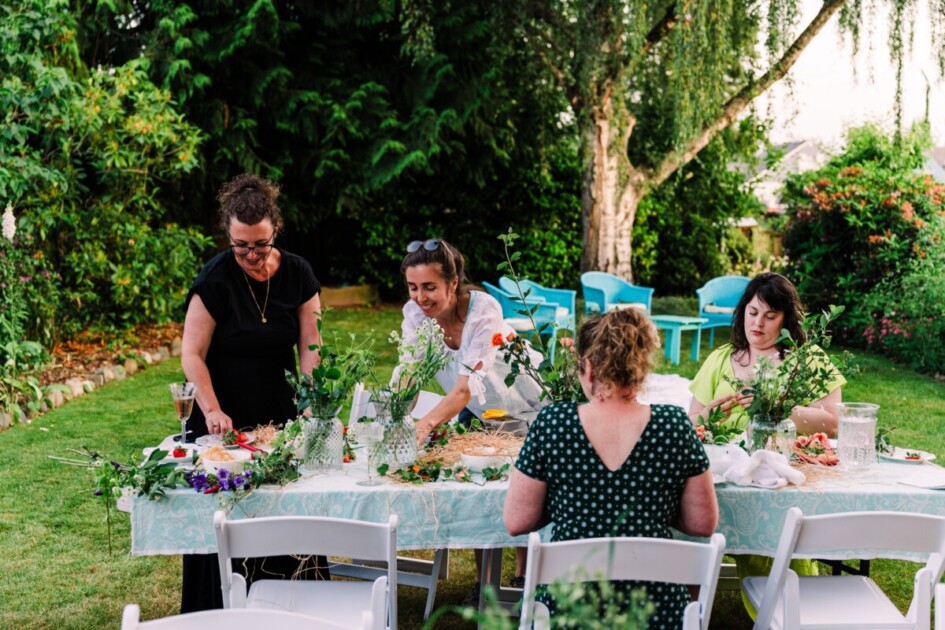 four women sit and stand at a table outside making flower bouquets--a great activity for a home bridal shower