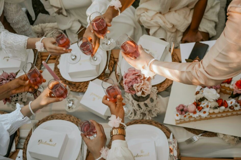 seven glasses of rose cheers over a table filled with bridesmaids boxes, flowers, and a cake at a home bridal shower
