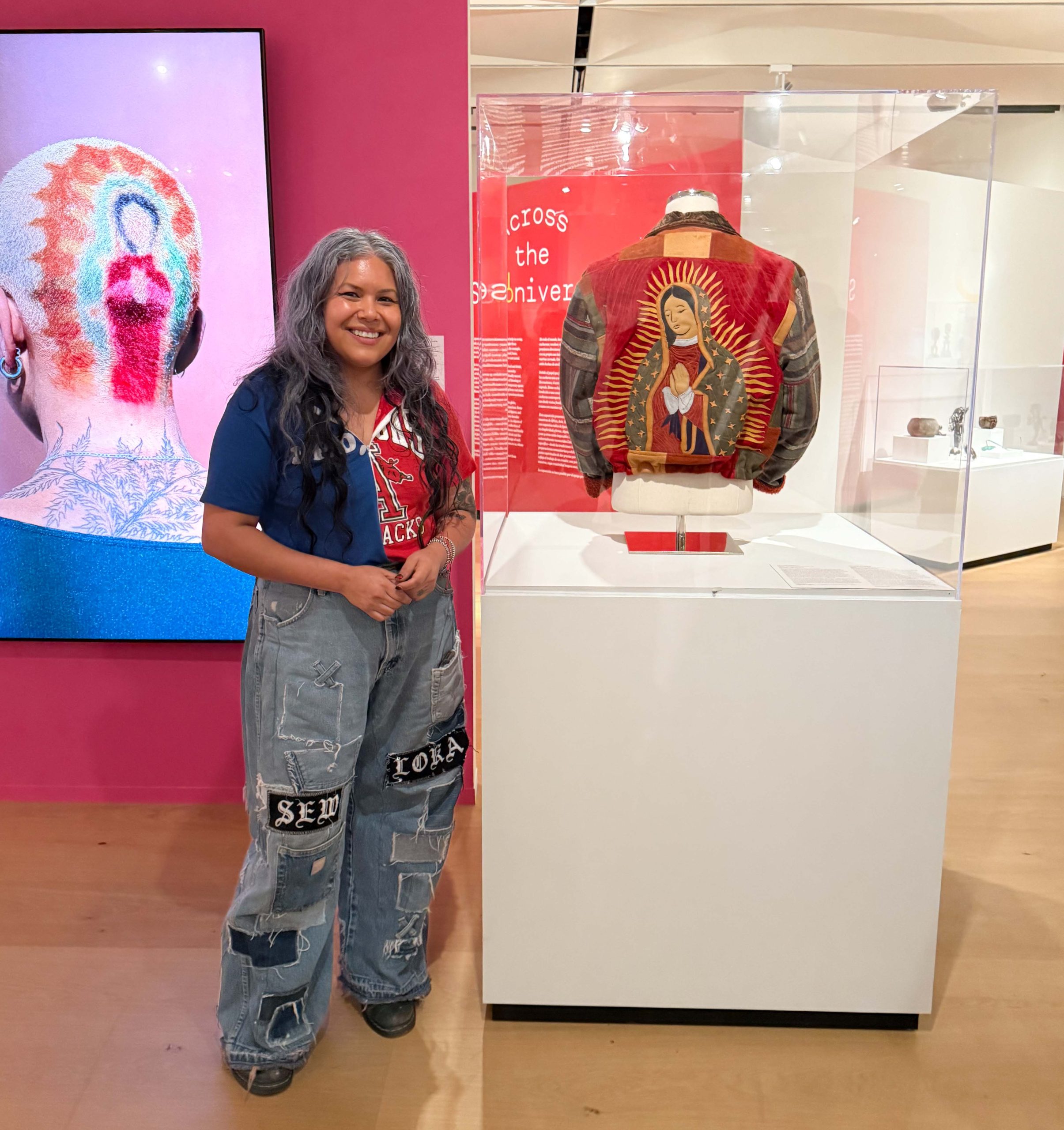 A person with jeans and a T-shirt stands in front of a colorful jacket with the Virgin of Guadalupe on the back.