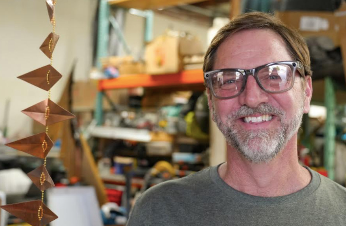 a portrait of artist Joseph Henseler with his works displayed behind him.