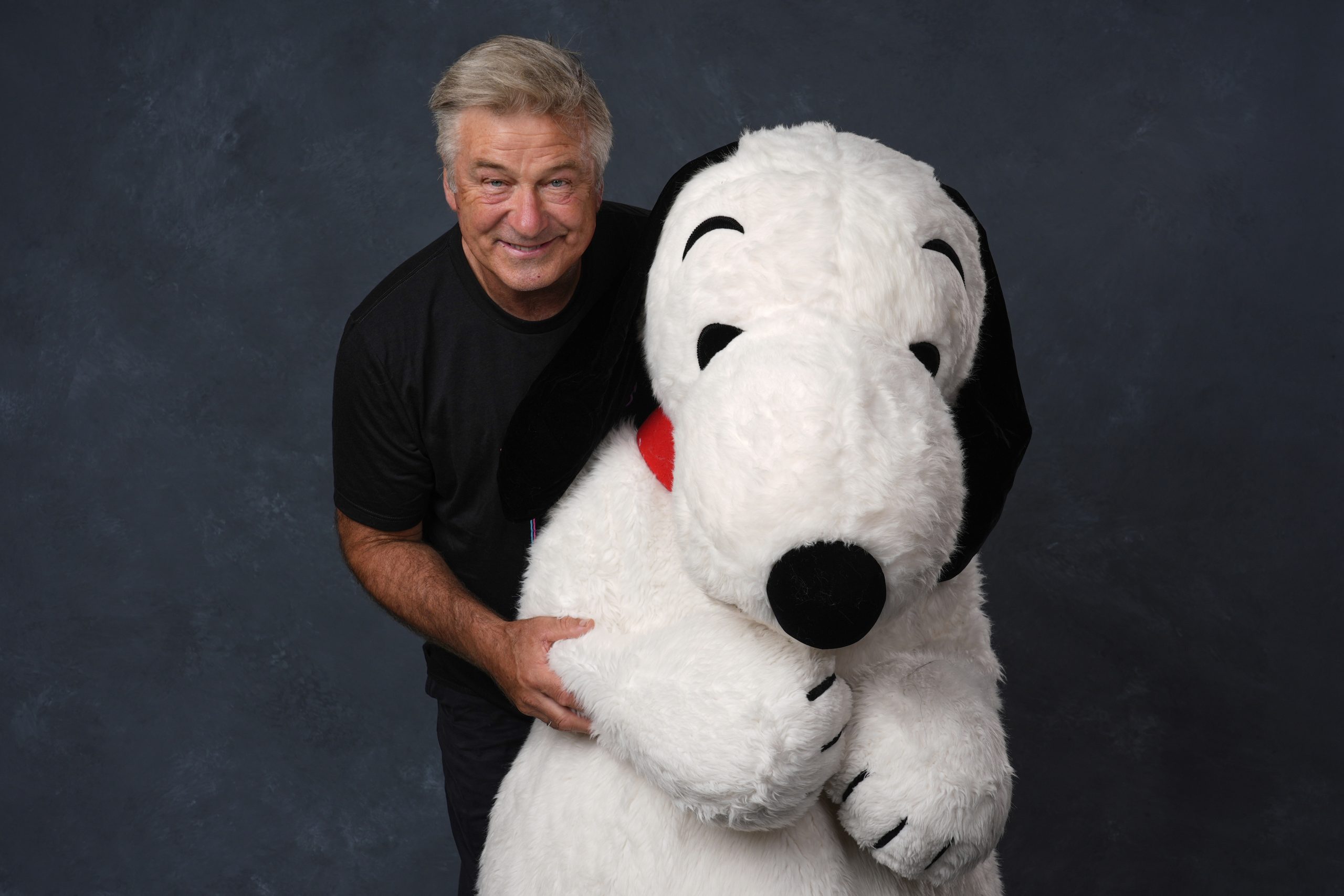 Actor Alec Baldwin peering out from behind a giant Snoopy plushie.