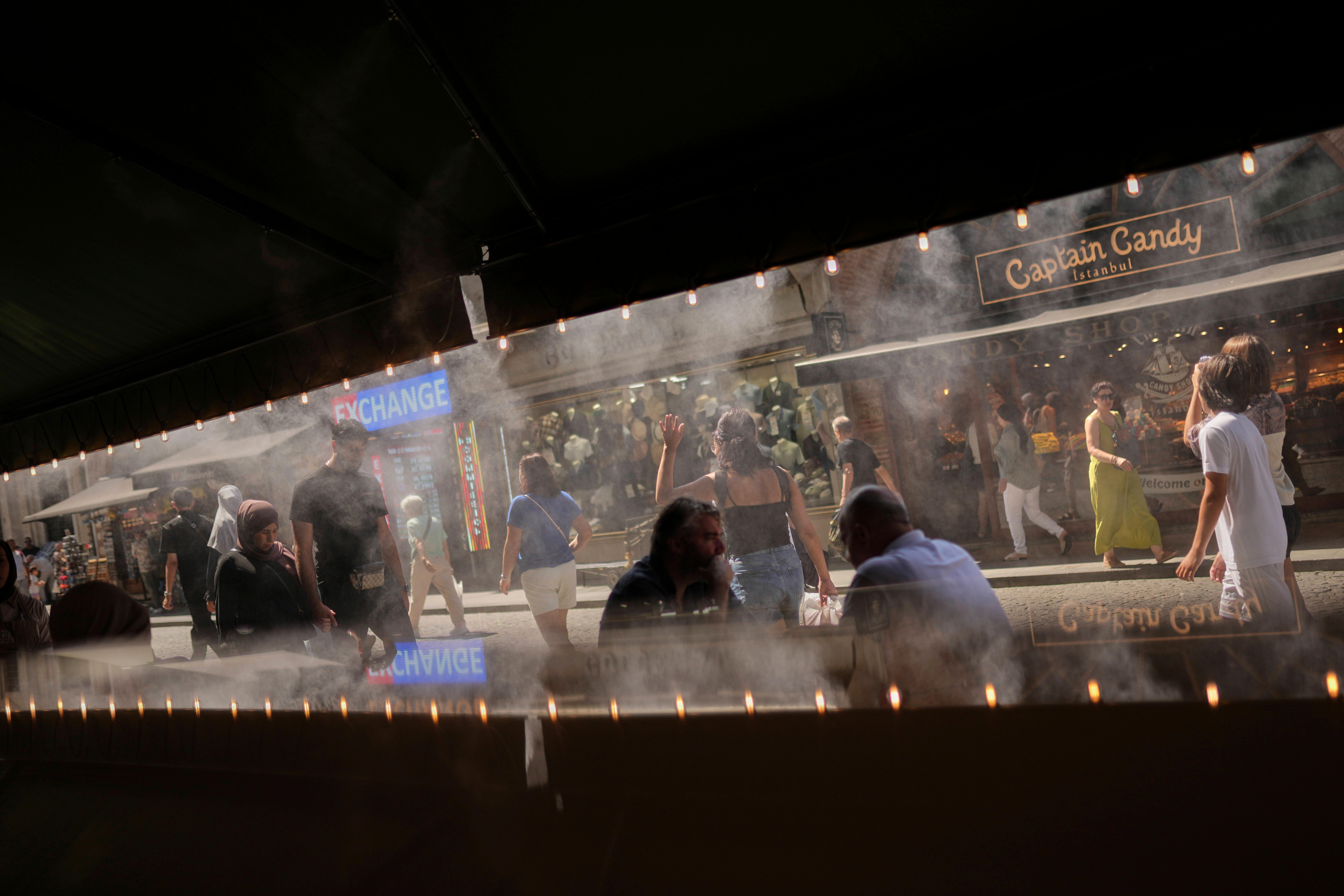 People walk past a coffee bar as water is sprayed...