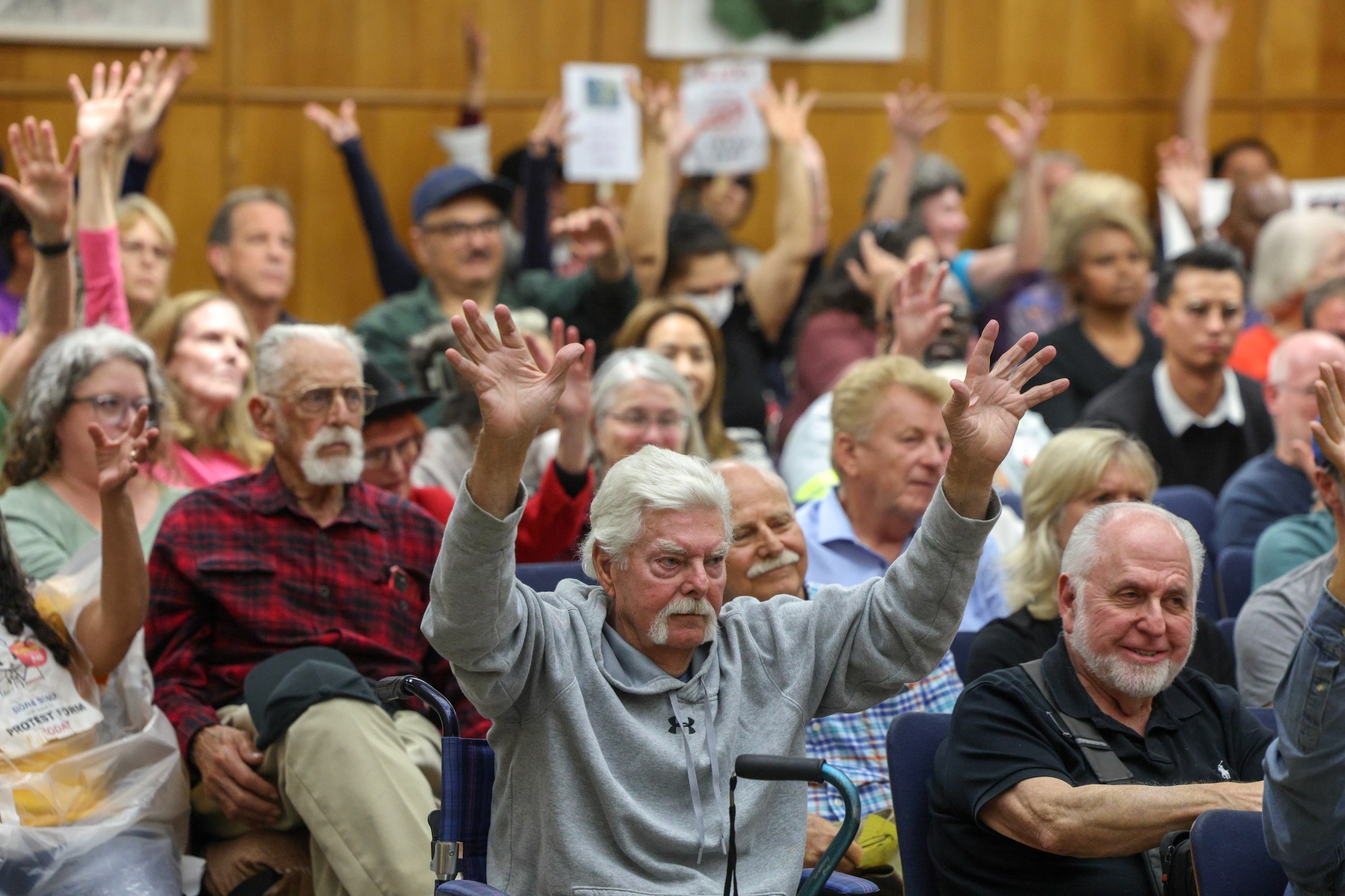 People wave their hands in support of a public commenter speaking in opposition to trash fee rate hikes during a San Diego City Council meeting at City Hall in San Diego on Monday, June 8, 2025. (Hayne Palmour IV / For The San Diego Union-Tribune)