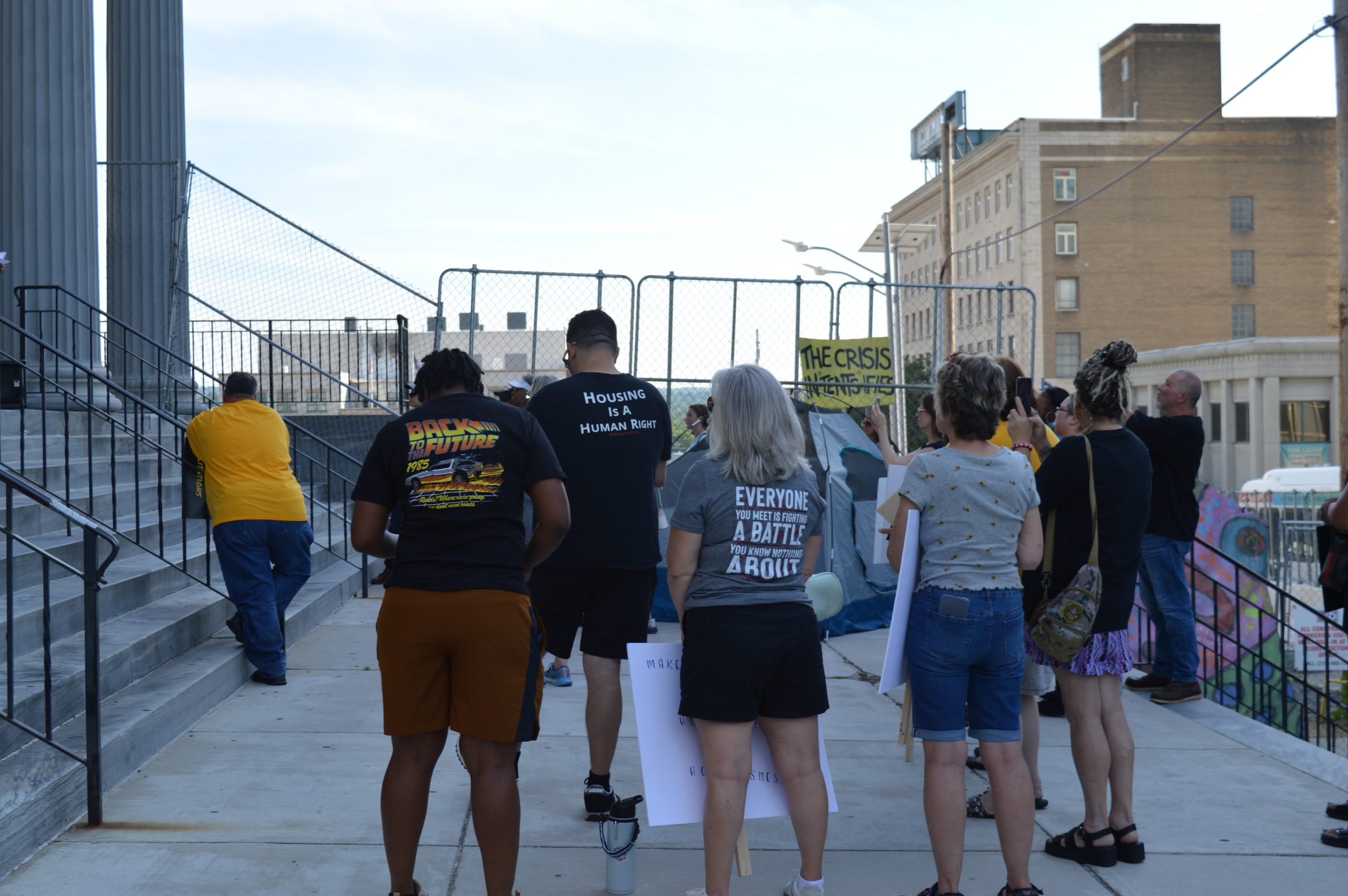 Attendees of a rally hold signs and listen to speakers...