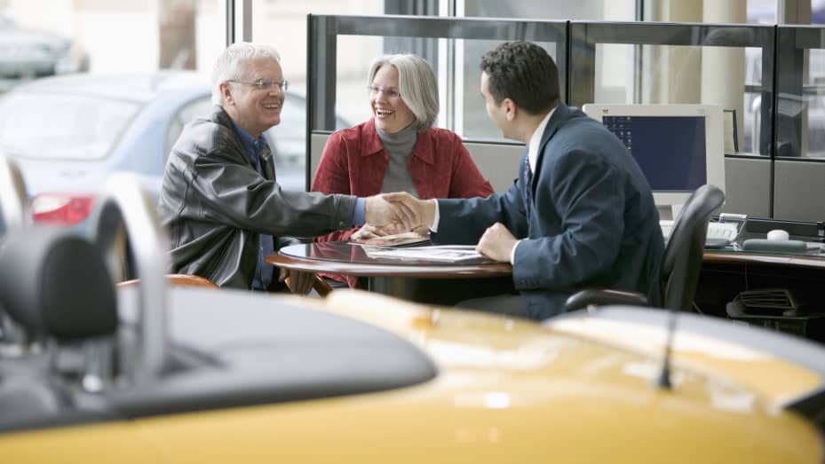 A couple sits at a desk across from a banker smiling and shaking hands.