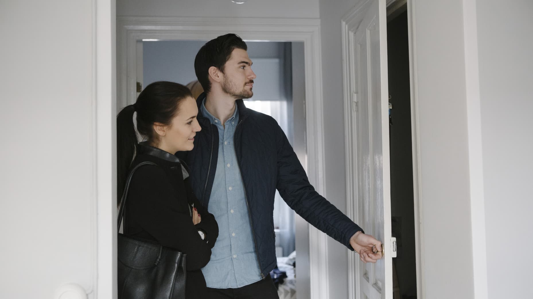 Young man opening door while standing with woman in corridor at home