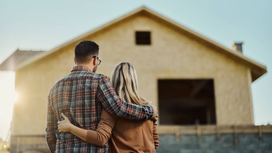 Rear view of an embraced couple looking at a house under construction.