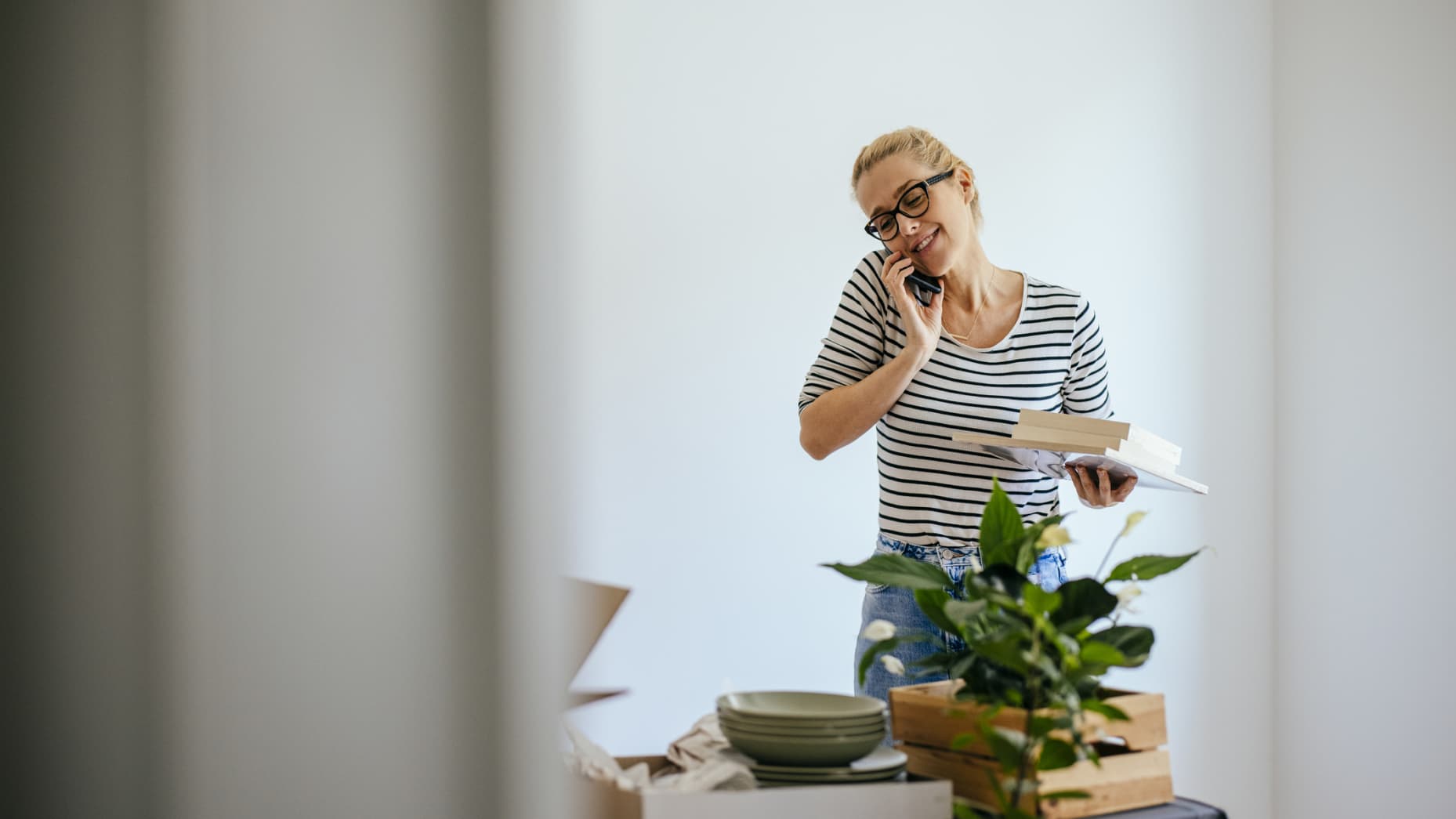 Beautiful blonde woman standing in the room. There are boxes in front of her. She is unpacking her things.