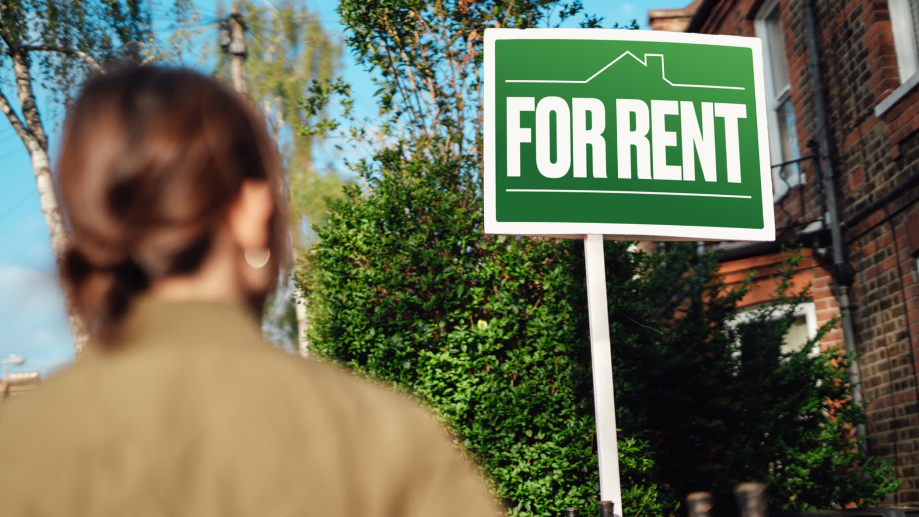 Woman looks at "For Rent" sign.