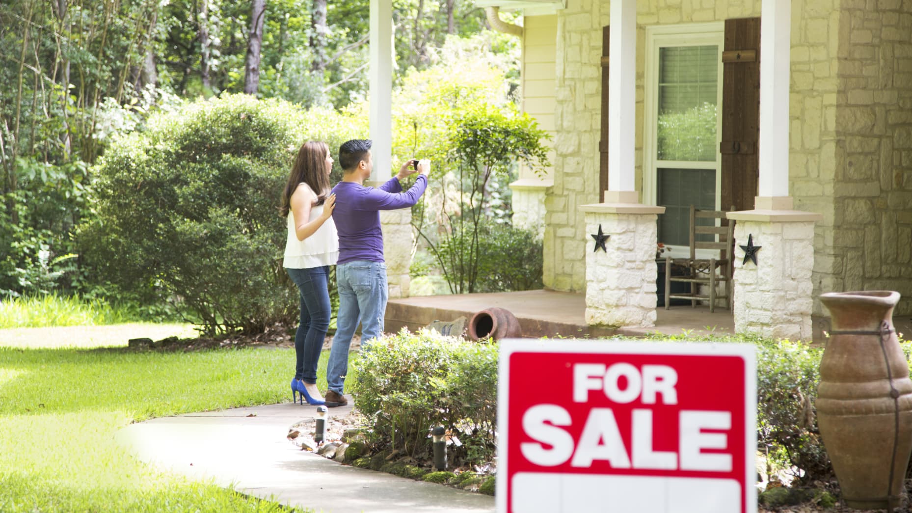 Adult couple are considering purchasing a new home. For sale sign in foreground.